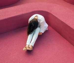 Woman sitting on a pink floor hugging her knees