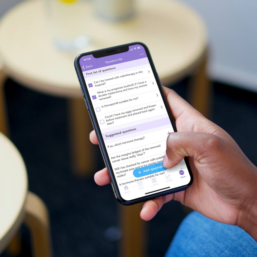 Woman sitting in front of a table with a coffee holding a phone showcasing OWise app suggested questions screenshot